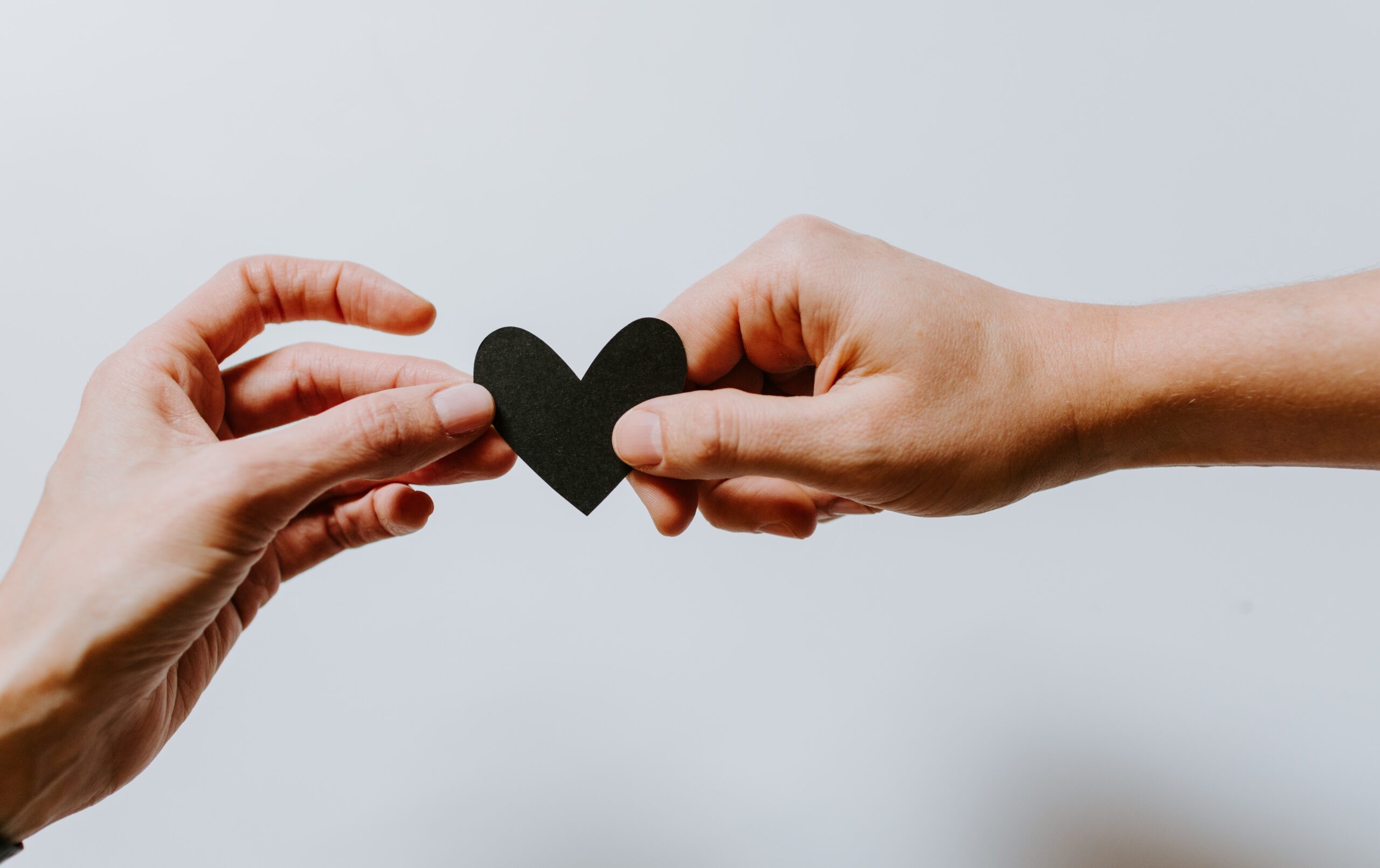 A hand giving a paper cutout of a black heart to another hand.